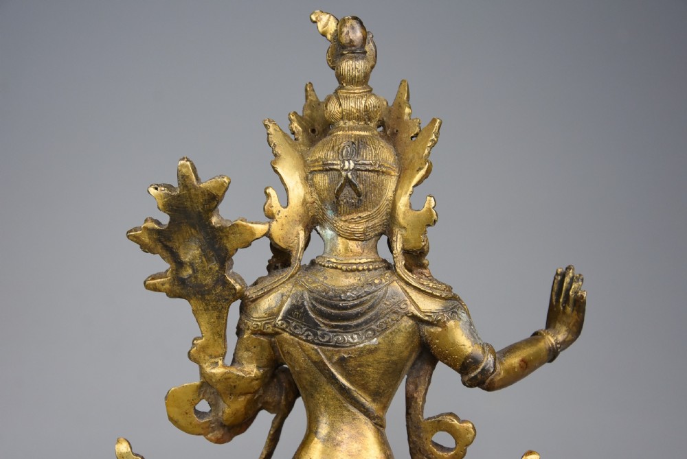 A seated gilt bronze figure of a Buddhist deity featuring an ornate crown, holding a lotus stem, with mineral inlays on a double-lotus base. View XI