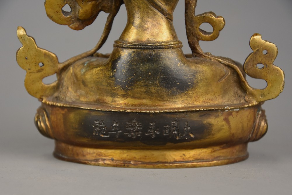 A seated gilt bronze figure of a Buddhist deity featuring an ornate crown, holding a lotus stem, with mineral inlays on a double-lotus base. View XII