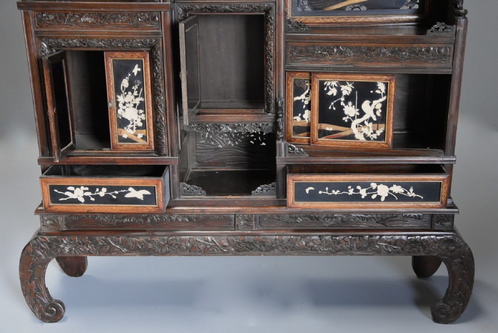 A late nineteenth-century Japanese Meiji period dark brown shodana cabinet featuring asymmetrical open shelves, carved foliage borders, and sliding cupboard doors inlaid with birds and flowers. View X