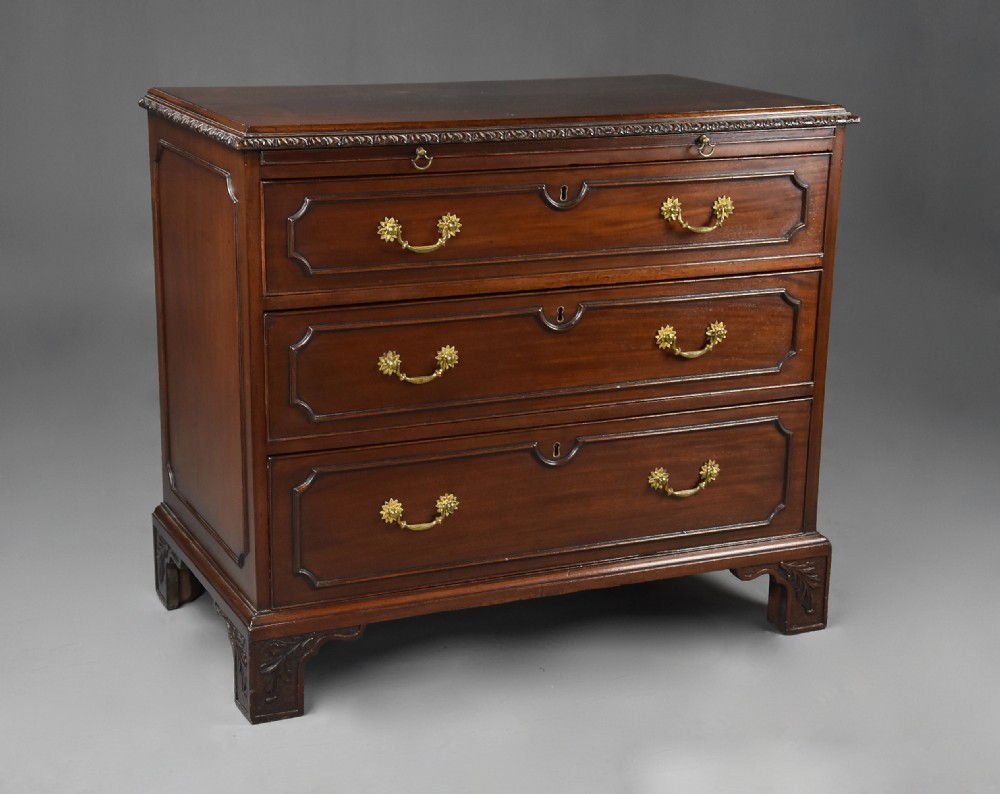 A late 19th-century dark mahogany chest of drawers featuring three graduated drawers, ornate brass swan-neck handles, a pull-out brushing slide, and carved bracket feet.