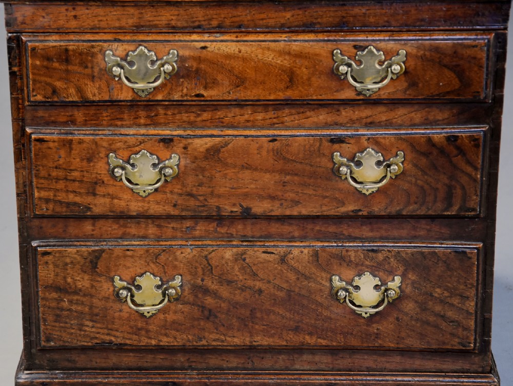 A late eighteenth-century warm brown elm wooden box designed in the form of a miniature chest of drawers with brass handles and bracket feet. View V
