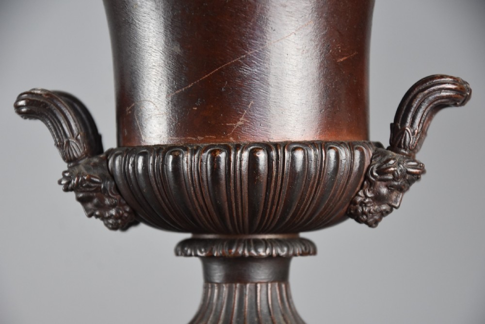 A pair of dark brown patinated spelter campana urns featuring gadrooned bases, scroll handles, and square stepped plinths with relief decoration. View VI