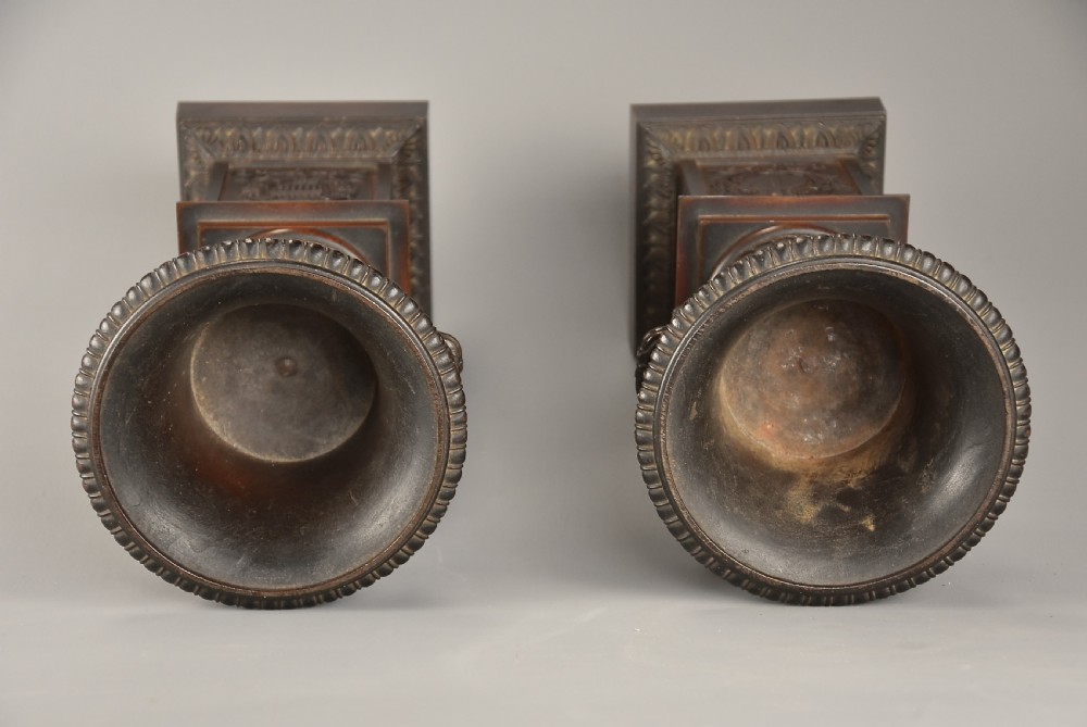 A pair of dark brown patinated spelter campana urns featuring gadrooned bases, scroll handles, and square stepped plinths with relief decoration. View IX