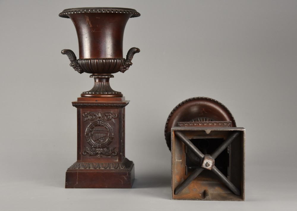 A pair of dark brown patinated spelter campana urns featuring gadrooned bases, scroll handles, and square stepped plinths with relief decoration. View X