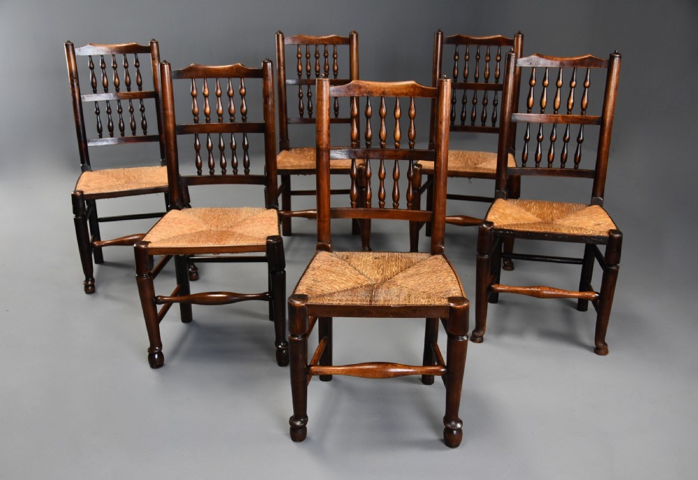 A set of six early nineteenth century ash and elm country dining chairs featuring turned spindle backrests and woven rush seats. View II