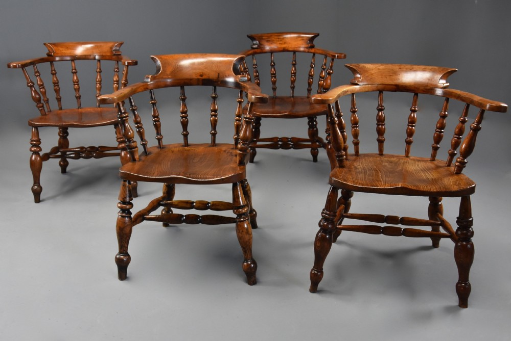 A set of four mid-19th-century Smokers Bow Windsor armchairs crafted from warm brown timber with turned spindles, sweeping armrests, and sculpted seats.