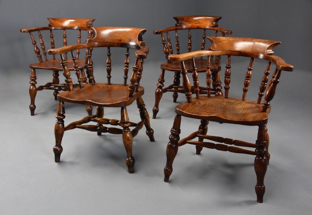 A set of four mid-19th-century Smokers Bow Windsor armchairs crafted from warm brown timber with turned spindles, sweeping armrests, and sculpted seats. View II