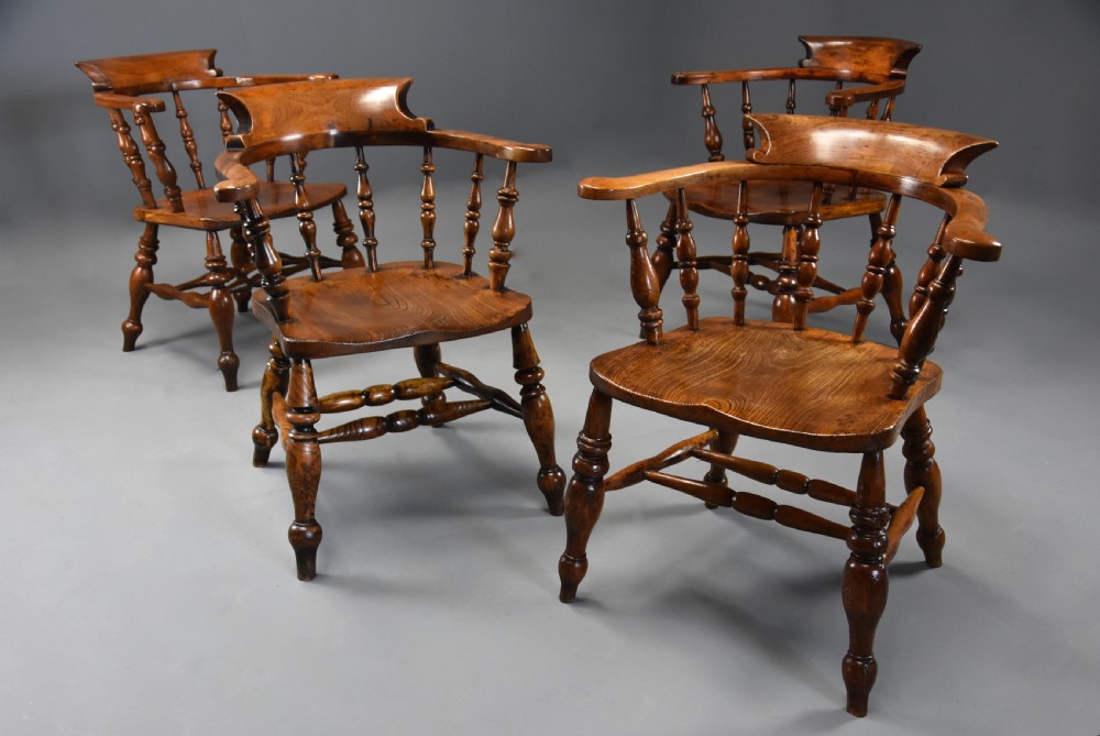 A set of four mid-19th-century Smokers Bow Windsor armchairs crafted from warm brown timber with turned spindles, sweeping armrests, and sculpted seats. View III