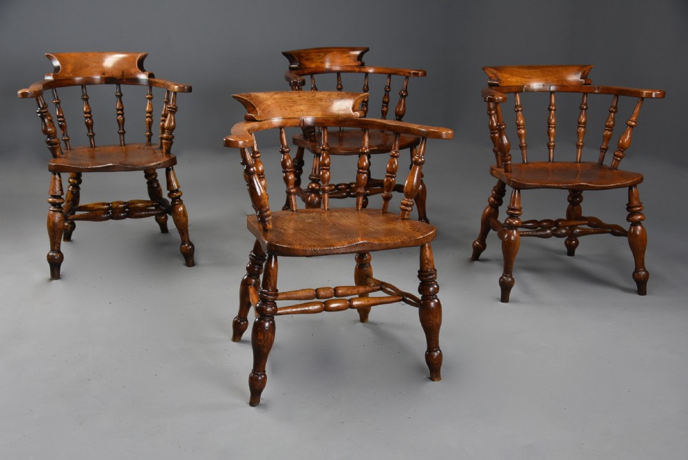 A set of four mid-19th-century Smokers Bow Windsor armchairs crafted from warm brown timber with turned spindles, sweeping armrests, and sculpted seats. View VI