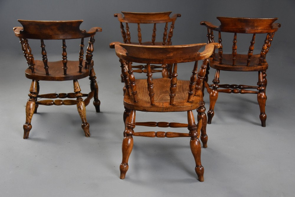 A set of four mid-19th-century Smokers Bow Windsor armchairs crafted from warm brown timber with turned spindles, sweeping armrests, and sculpted seats. View XI