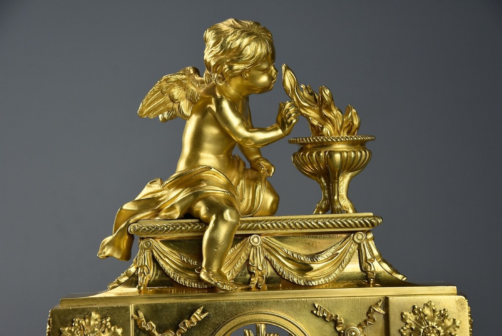 A pair of late nineteenth-century gilded bronze fire dogs featuring seated winged cherubs warming their hands by flaming urns above solar masks and drapery. View VII