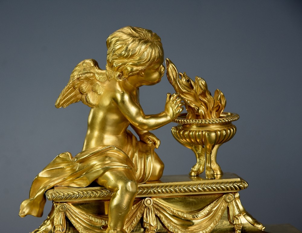 A pair of late nineteenth-century gilded bronze fire dogs featuring seated winged cherubs warming their hands by flaming urns above solar masks and drapery. View VIII