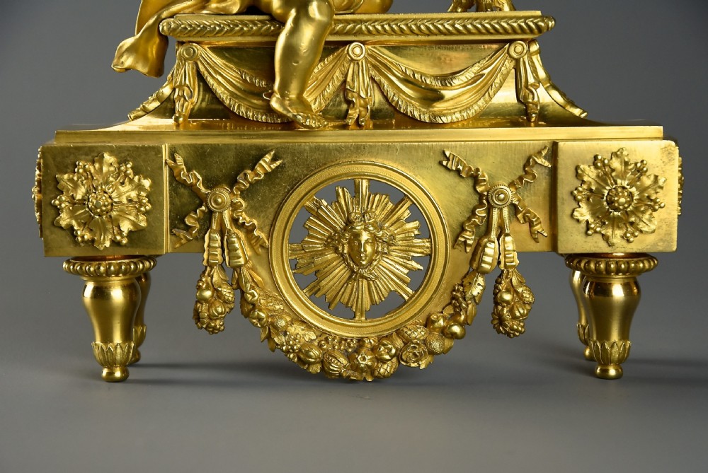 A pair of late nineteenth-century gilded bronze fire dogs featuring seated winged cherubs warming their hands by flaming urns above solar masks and drapery. View IX