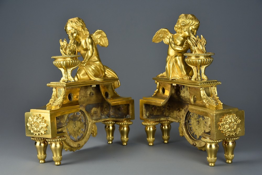 A pair of late nineteenth-century gilded bronze fire dogs featuring seated winged cherubs warming their hands by flaming urns above solar masks and drapery. View XIII