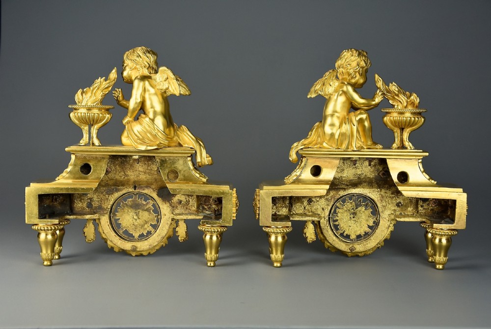 A pair of late nineteenth-century gilded bronze fire dogs featuring seated winged cherubs warming their hands by flaming urns above solar masks and drapery. View XIV