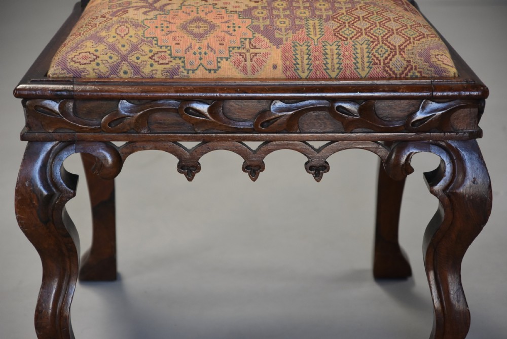 A pair of mid-19th century carved rosewood Gothic Revival hall chairs featuring pointed arch backs, decorative finials, patterned fabric upholstery, and cabriole legs. View X