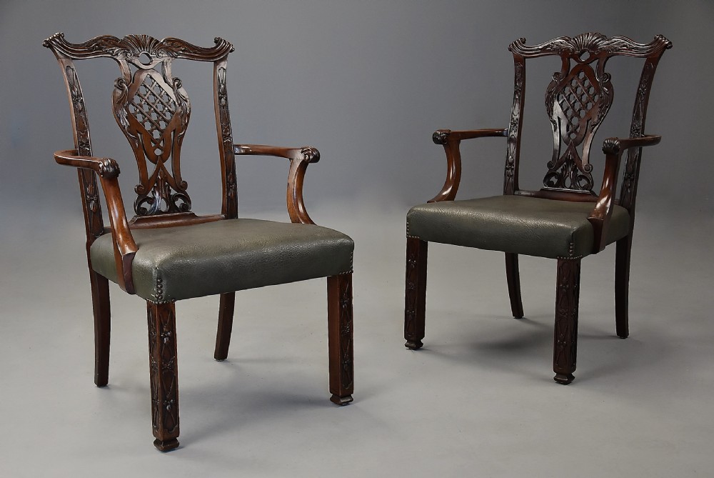A pair of late nineteenth century mahogany open armchairs featuring carved pierced splat backs and dark green leather upholstered seats.