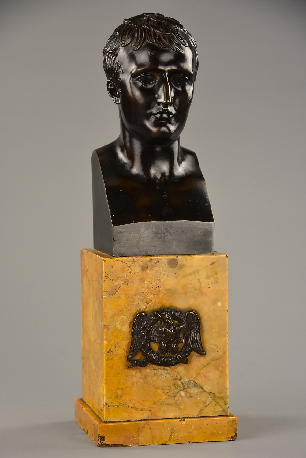 A dark patinated bronze bust of Napoleon Bonaparte mounted on a yellow marble plinth decorated with a bronze eagle mount.