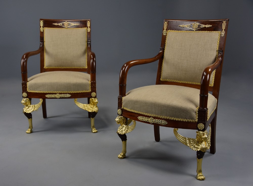 A pair of late 19th-century French mahogany open armchairs featuring gilt-bronze winged lion monopodia legs and beige fabric upholstery.