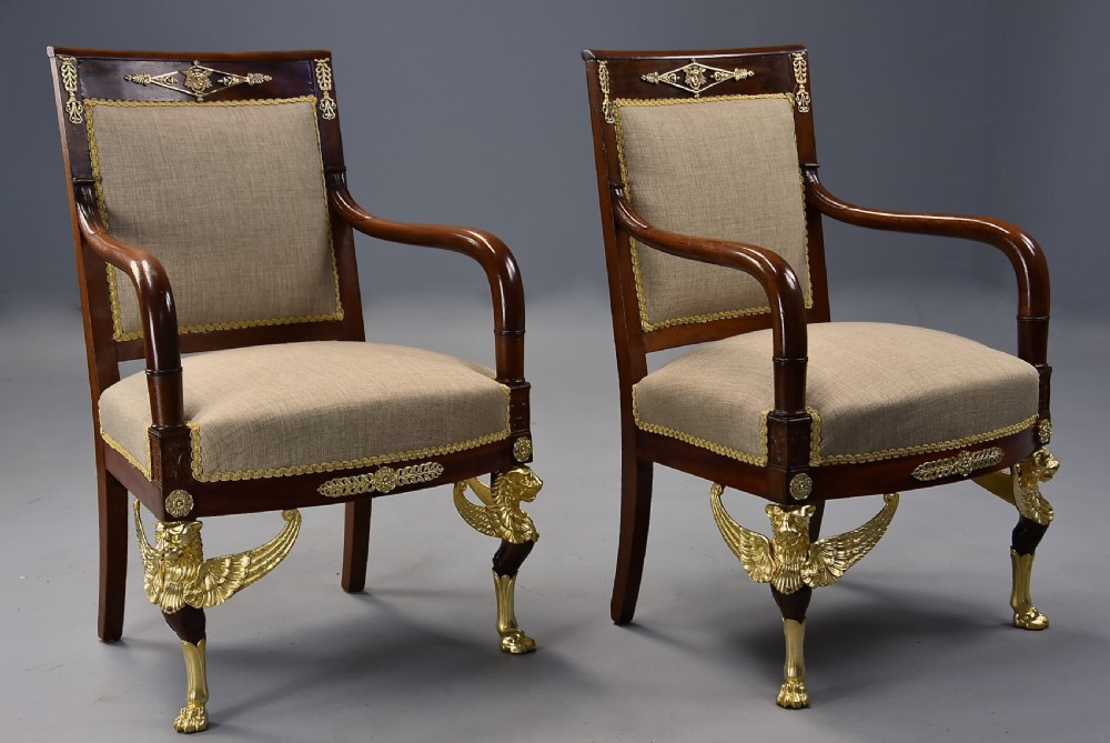 A pair of late 19th-century French mahogany open armchairs featuring gilt-bronze winged lion monopodia legs and beige fabric upholstery. View V