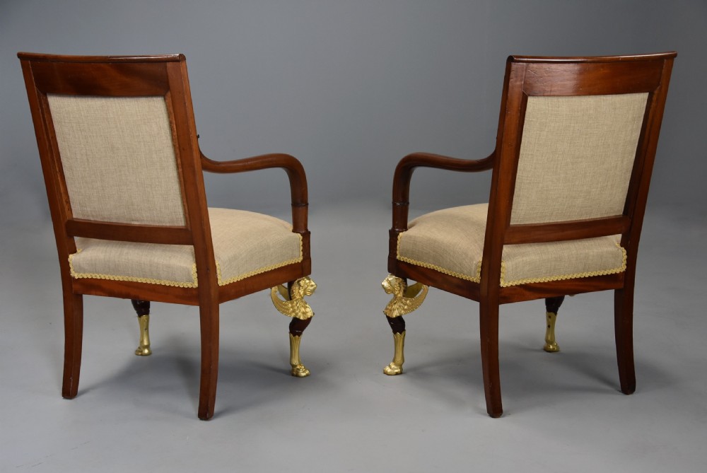 A pair of late 19th-century French mahogany open armchairs featuring gilt-bronze winged lion monopodia legs and beige fabric upholstery. View XIV