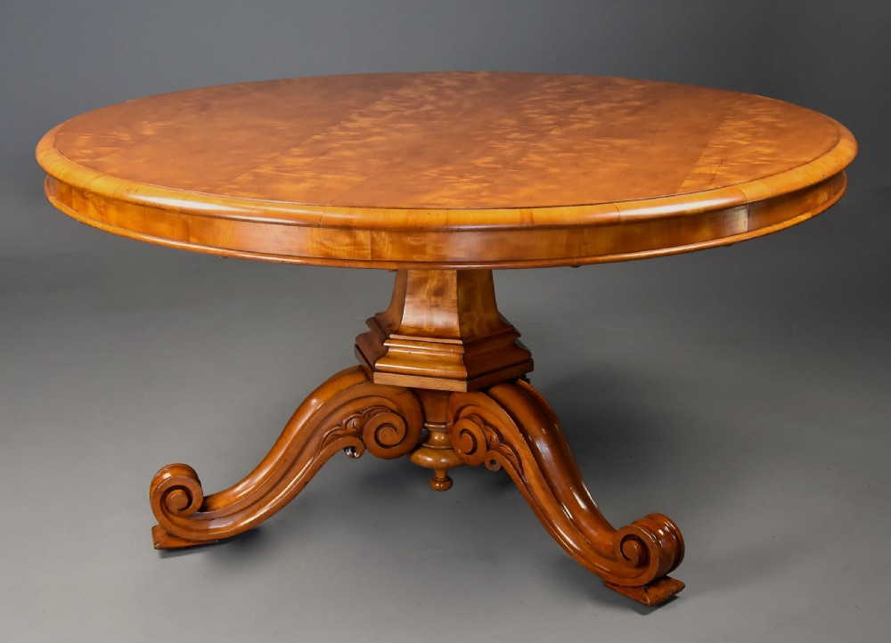 A circular mid-19th-century tilt-top breakfast table made from figured satin birch timber with a carved central pedestal base and scroll feet. View IV