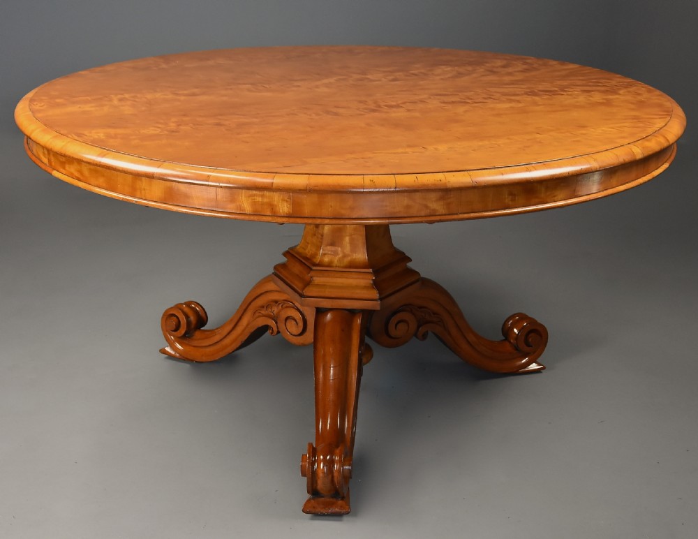 A circular mid-19th-century tilt-top breakfast table made from figured satin birch timber with a carved central pedestal base and scroll feet. View V