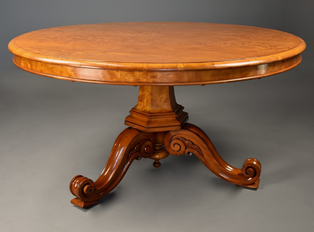 A circular mid-19th-century tilt-top breakfast table made from figured satin birch timber with a carved central pedestal base and scroll feet. View VI