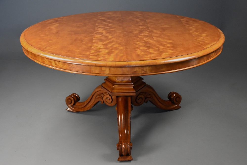 A circular mid-19th-century tilt-top breakfast table made from figured satin birch timber with a carved central pedestal base and scroll feet. View VII