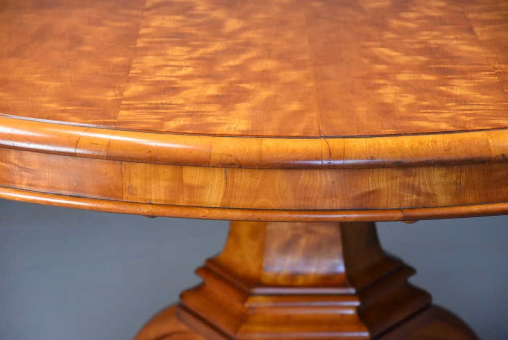 A circular mid-19th-century tilt-top breakfast table made from figured satin birch timber with a carved central pedestal base and scroll feet. View VIII