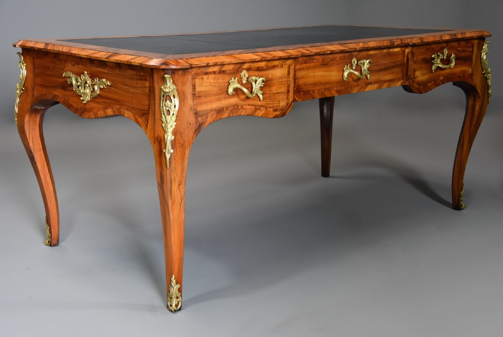 A mid-19th-century French style bureau plat desk crafted from goncalo alves wood featuring a black leather inset top, three frieze drawers, ornate gilt-bronze mounts, and cabriole legs.