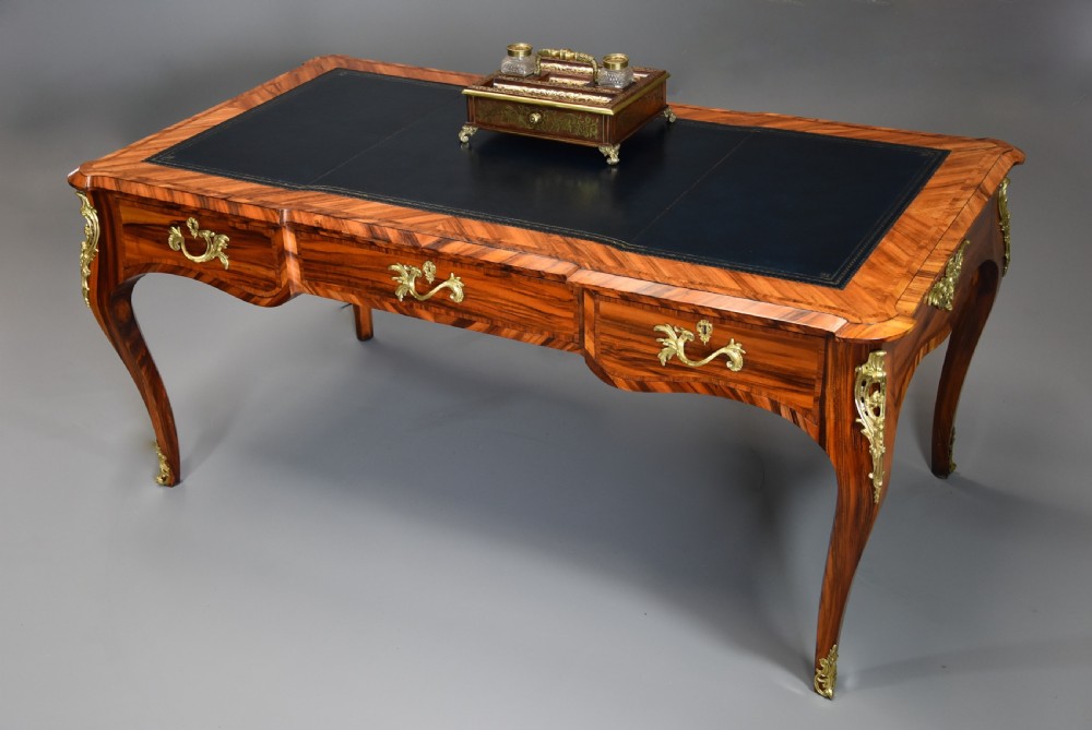 A mid-19th-century French style bureau plat desk crafted from goncalo alves wood featuring a black leather inset top, three frieze drawers, ornate gilt-bronze mounts, and cabriole legs. View III