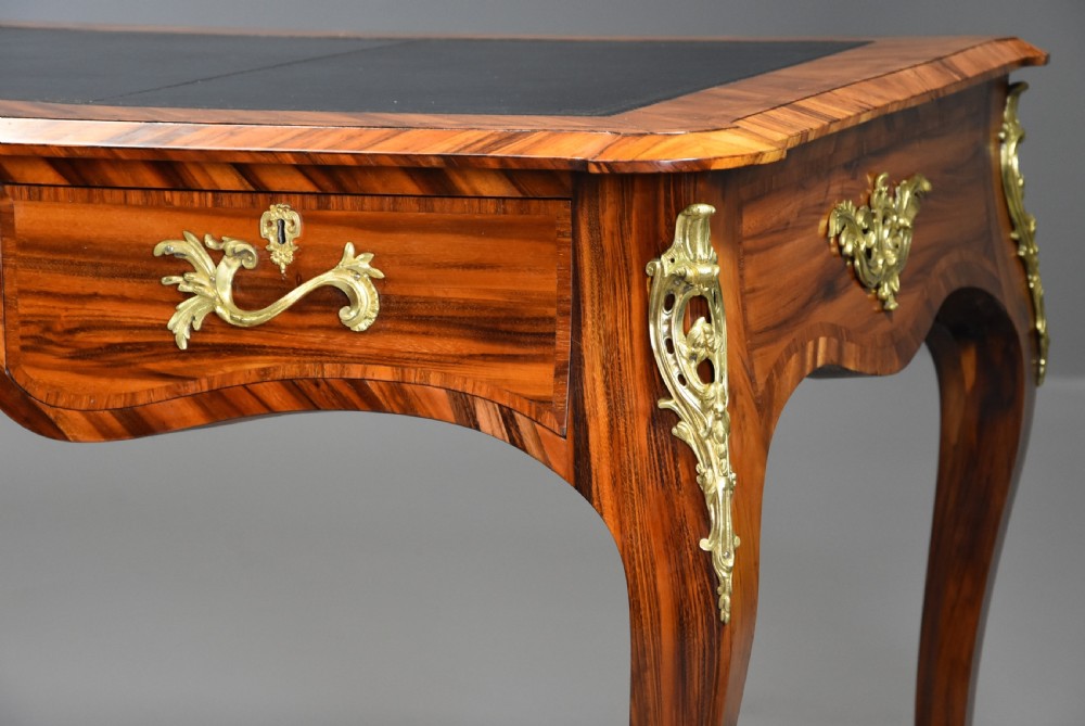 A mid-19th-century French style bureau plat desk crafted from goncalo alves wood featuring a black leather inset top, three frieze drawers, ornate gilt-bronze mounts, and cabriole legs. View VI