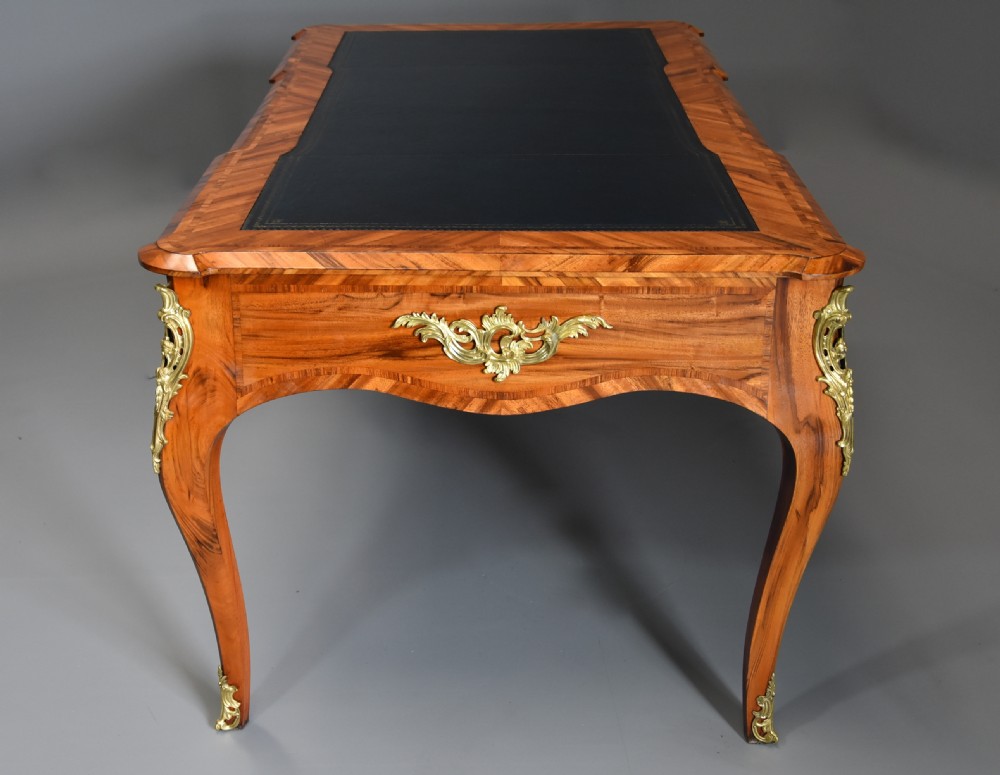 A mid-19th-century French style bureau plat desk crafted from goncalo alves wood featuring a black leather inset top, three frieze drawers, ornate gilt-bronze mounts, and cabriole legs. View IX
