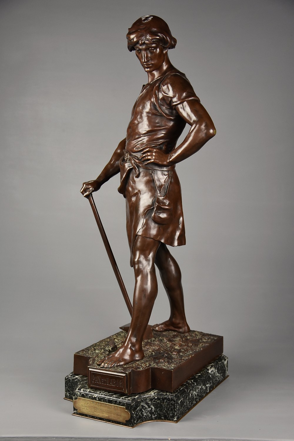 A dark brown patinated bronze sculpture of a standing male figure resting on a rectangular marble base with an etched metal title plaque.