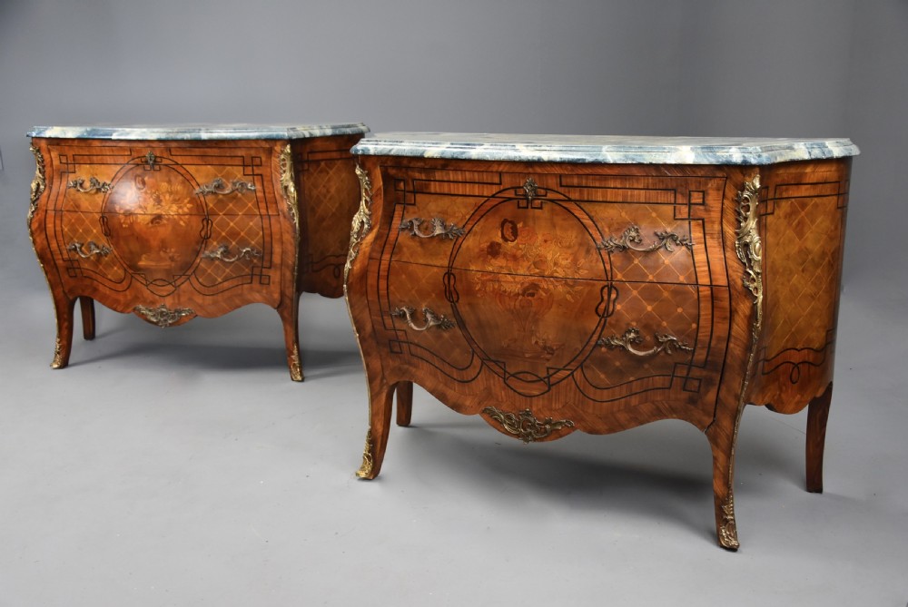 A pair of early 20th century French kingwood bombe commodes with floral marquetry inlay, gilt-bronze mounts, and marble tops.