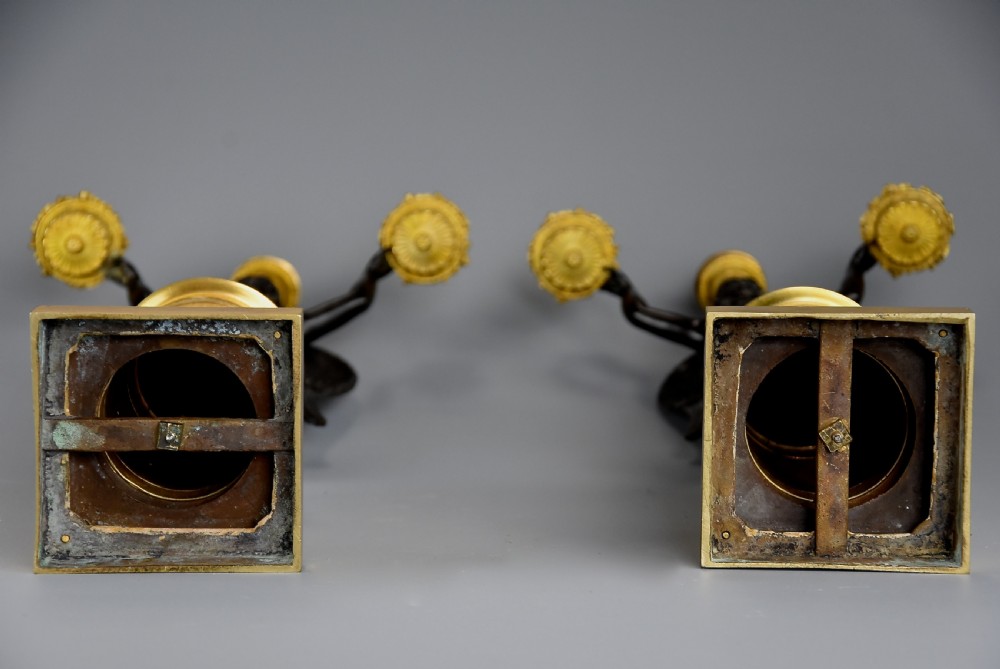 A pair of early nineteenth-century French Empire patinated and gilt bronze candelabra featuring winged classical figures holding candle nozzles aloft on decorated cylindrical pedestals. View XIV