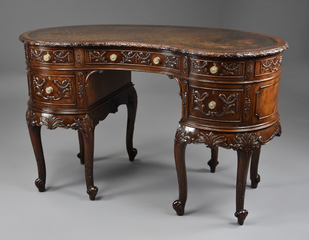 An Edwardian carved mahogany kidney-shaped desk featuring an inset leather writing top, ornate carved drawer fronts, and cabriole legs.