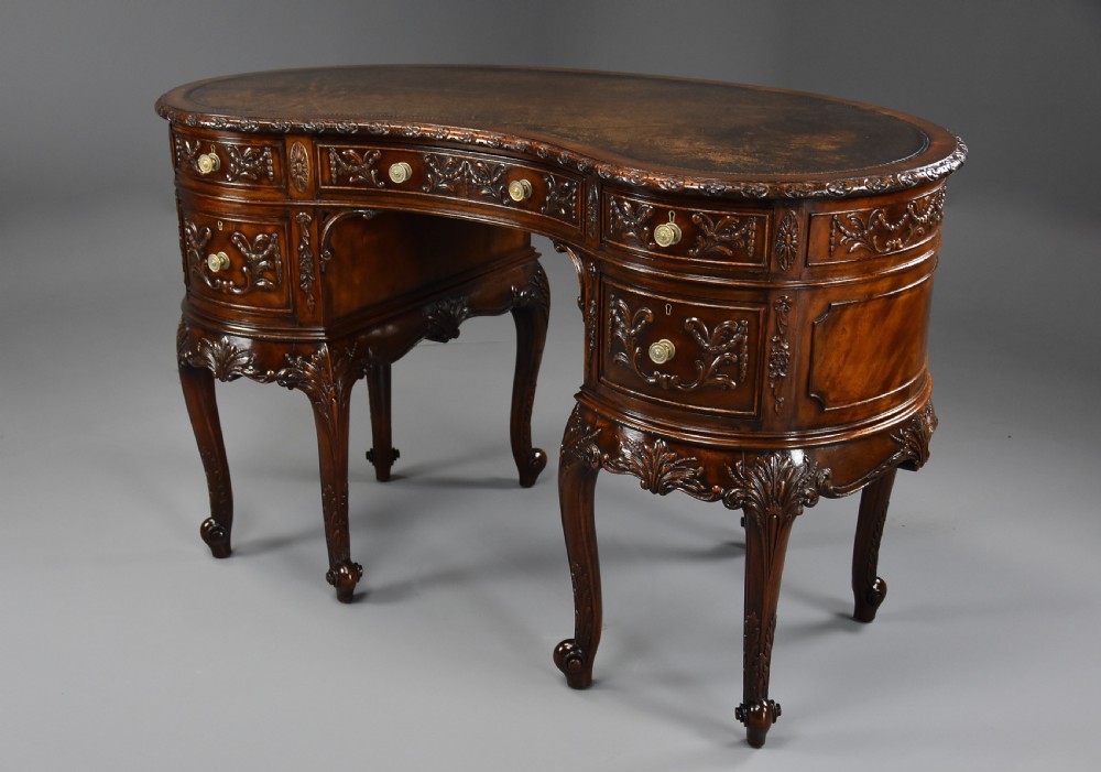 An Edwardian carved mahogany kidney-shaped desk featuring an inset leather writing top, ornate carved drawer fronts, and cabriole legs. View IV