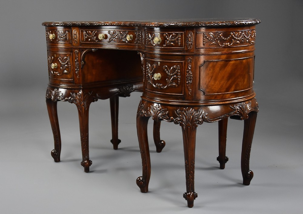 An Edwardian carved mahogany kidney-shaped desk featuring an inset leather writing top, ornate carved drawer fronts, and cabriole legs. View V