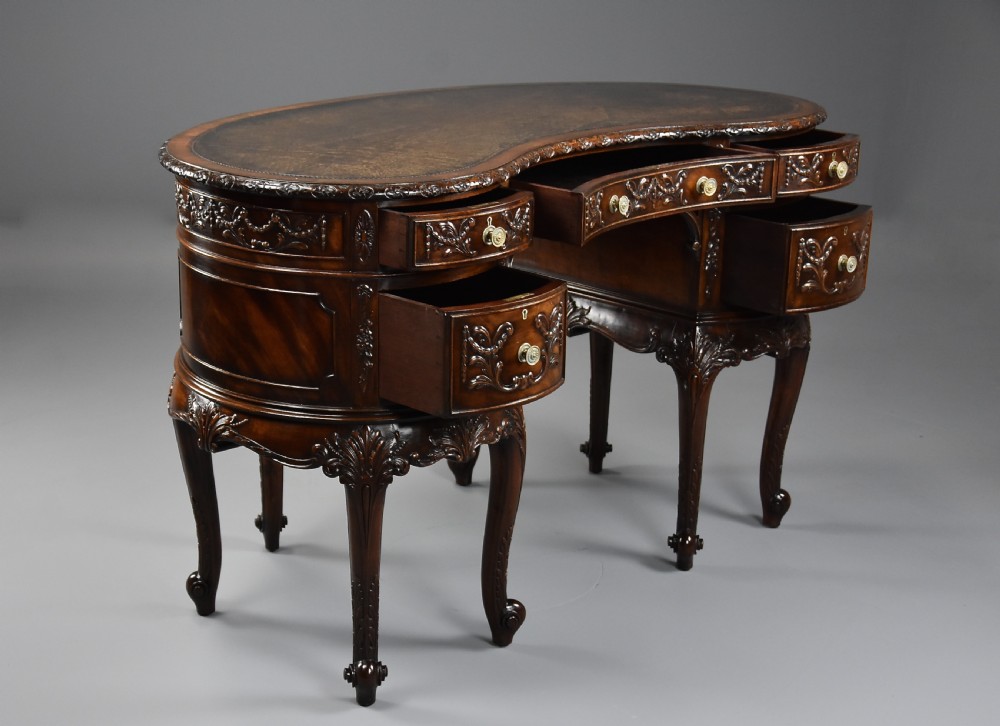 An Edwardian carved mahogany kidney-shaped desk featuring an inset leather writing top, ornate carved drawer fronts, and cabriole legs. View VI
