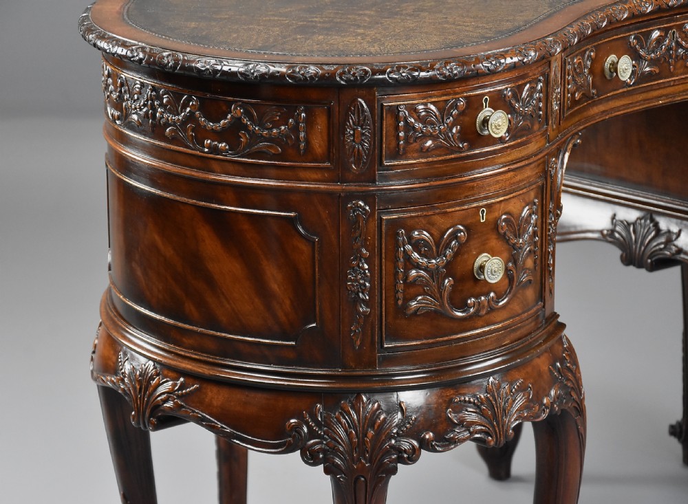 An Edwardian carved mahogany kidney-shaped desk featuring an inset leather writing top, ornate carved drawer fronts, and cabriole legs. View VII