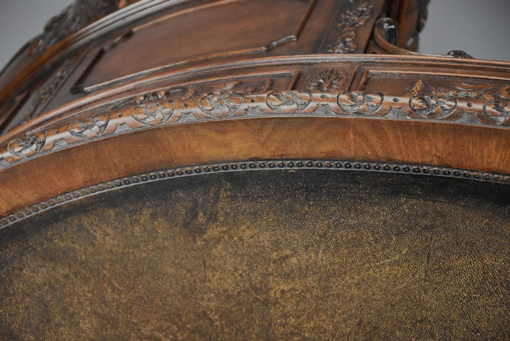 An Edwardian carved mahogany kidney-shaped desk featuring an inset leather writing top, ornate carved drawer fronts, and cabriole legs. View X