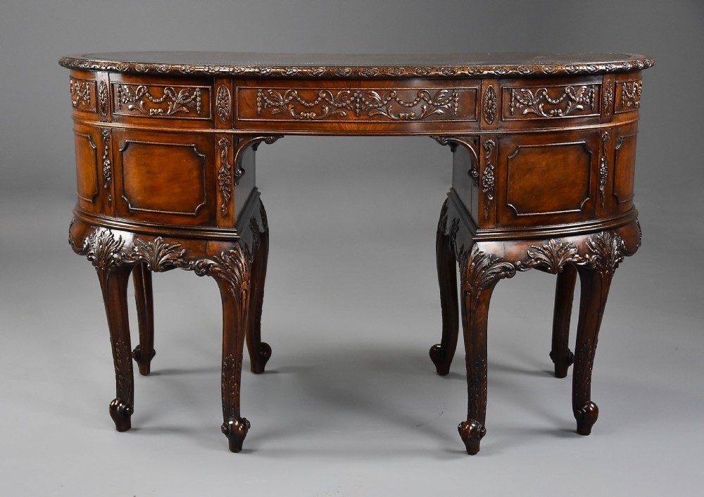 An Edwardian carved mahogany kidney-shaped desk featuring an inset leather writing top, ornate carved drawer fronts, and cabriole legs. View XII