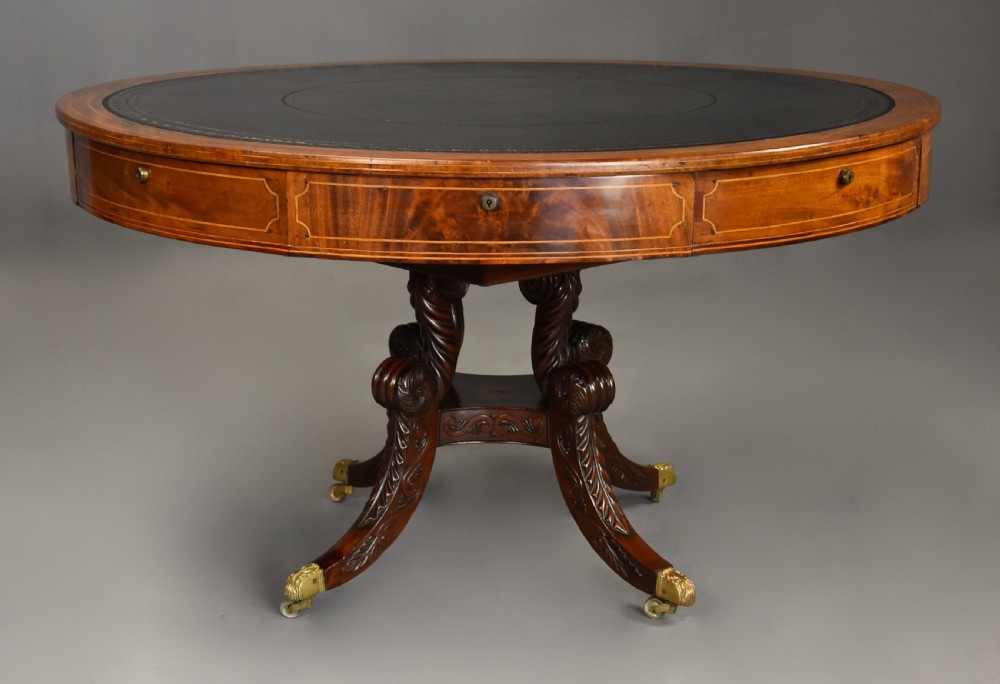 An early 19th-century circular mahogany Regency drum table featuring a dark leather inset top, frieze drawers with line inlay, and a carved central pedestal supported by four scroll legs on brass castors. View II