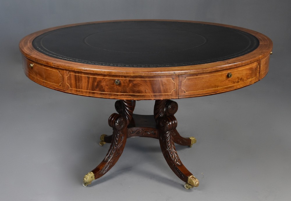 An early 19th-century circular mahogany Regency drum table featuring a dark leather inset top, frieze drawers with line inlay, and a carved central pedestal supported by four scroll legs on brass castors. View III