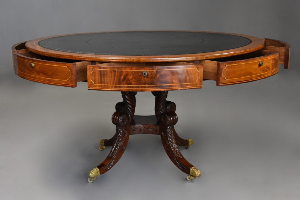An early 19th-century circular mahogany Regency drum table featuring a dark leather inset top, frieze drawers with line inlay, and a carved central pedestal supported by four scroll legs on brass castors. View VIII