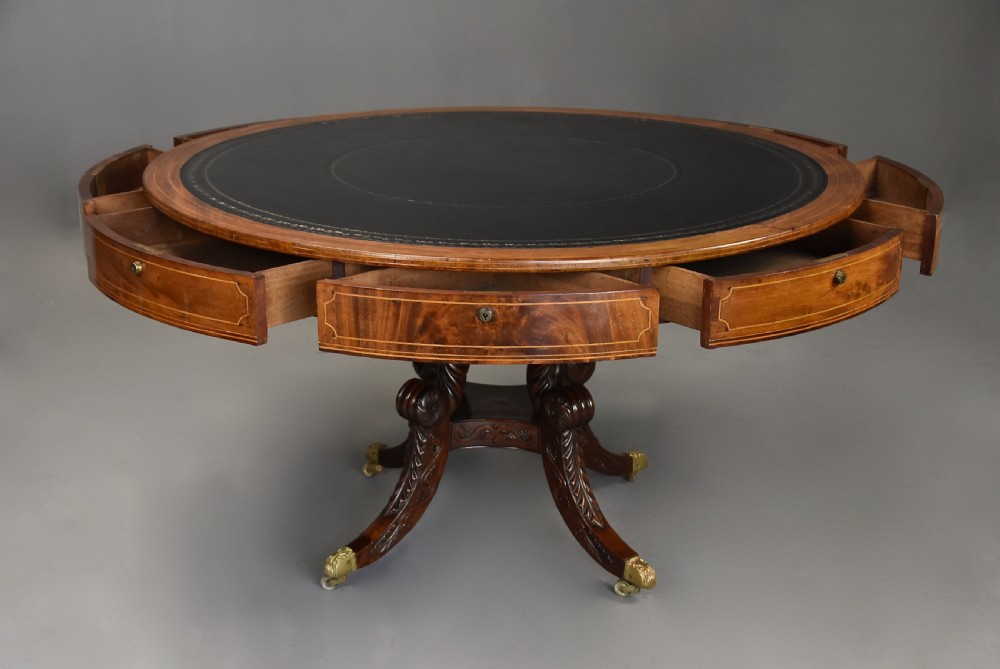 An early 19th-century circular mahogany Regency drum table featuring a dark leather inset top, frieze drawers with line inlay, and a carved central pedestal supported by four scroll legs on brass castors. View IX