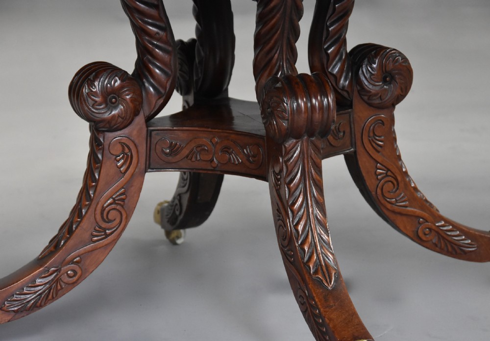An early 19th-century circular mahogany Regency drum table featuring a dark leather inset top, frieze drawers with line inlay, and a carved central pedestal supported by four scroll legs on brass castors. View XVI