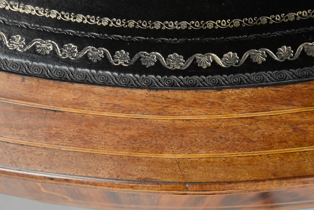 An early 19th-century circular mahogany Regency drum table featuring a dark leather inset top, frieze drawers with line inlay, and a carved central pedestal supported by four scroll legs on brass castors. View XIX